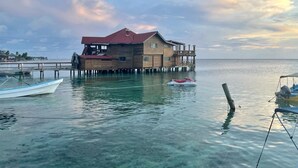 A wooden house on stilts over clear water, connected by a dock. - Less than 2 minute walk to beach in half moon bay and main strip in west end (West End)