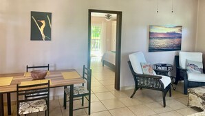 A dining area with a wooden table and chairs, a ceiling fan, and a painting of a sunset. - Less than 2 minute walk to beach in half moon bay and main strip in west end (West End)