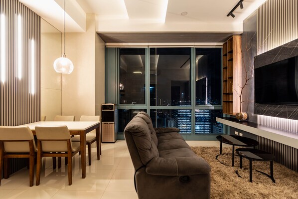 A modern living room with a sofa, dining table, chairs, and a TV mounted on the wall. - Luxury 2BR Gem in One Uptown, bgc (Taguig)