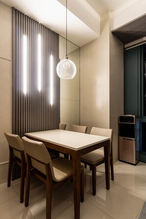 A modern dining area with a rectangular table and six chairs, a hanging pendant light, and a built-in water dispenser. - Luxury 2BR Gem in One Uptown, bgc (Taguig)