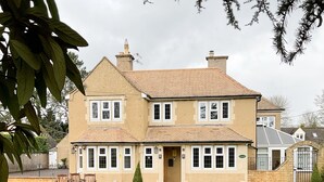 A two-story house with a large front lawn, a stone entrance, and a brick chimney. - Southlands B&B (Cheltenham)