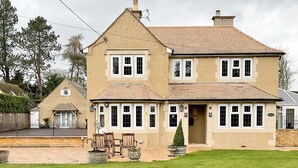 A two-story house with a tiled roof, a front porch with wooden chairs, and a well-maintained lawn. - Southlands B&B (Cheltenham)