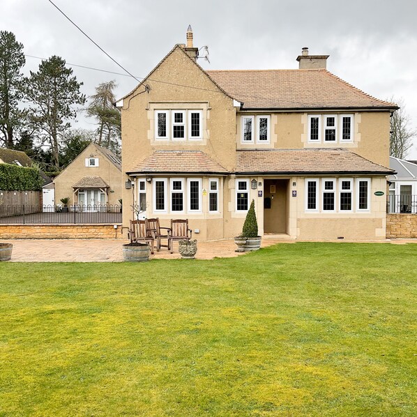 A two-story house with a tiled roof, a front porch with wooden chairs, and a well-maintained lawn. - Southlands B&B (Cheltenham)