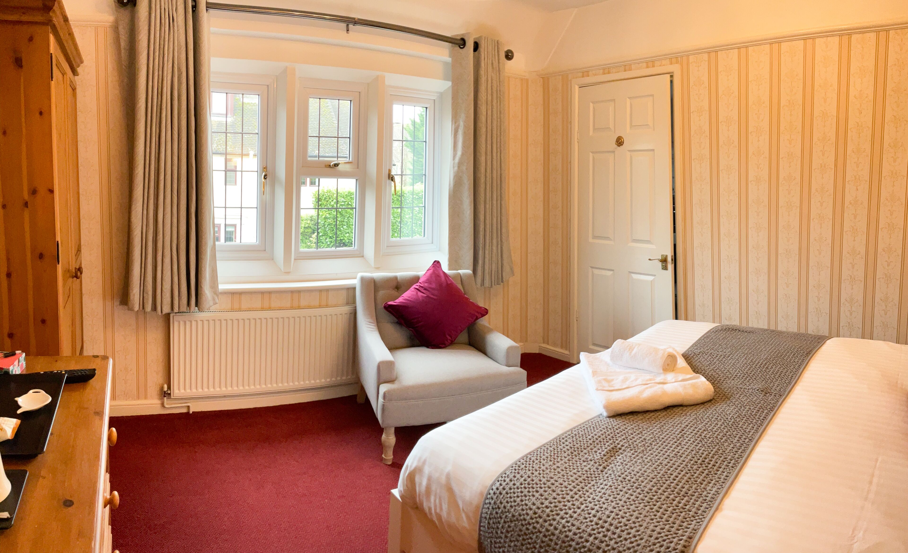 Een slaapkamer met een groot bed, een stoel, een raam met gordijnen, een radiator en een deur.