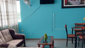A living room with a teal wall, a flat-screen TV, a painting, a dining table with chairs, and a sofa.