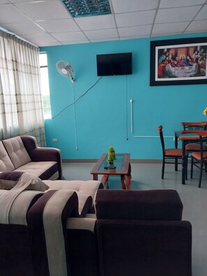 Ein Wohnzimmer mit einer türkisfarbenen Wand, einem Flachbildfernseher, einem Gemälde, einem Esstisch mit Stühlen und einem Sofa.