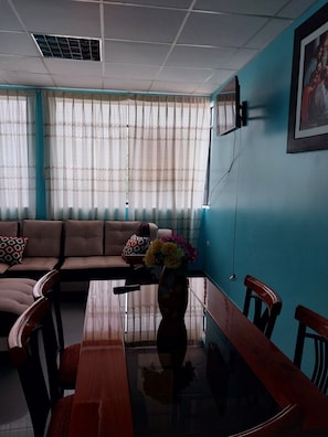 A living room with a sofa, a dining table, and a vase with flowers.