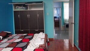 A bedroom with a bed, a wardrobe, a fan, and a door leading to another room.