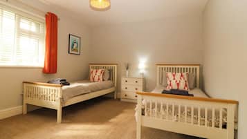A bedroom with two single beds, a nightstand, a lamp, a radiator, and a window with curtains.
