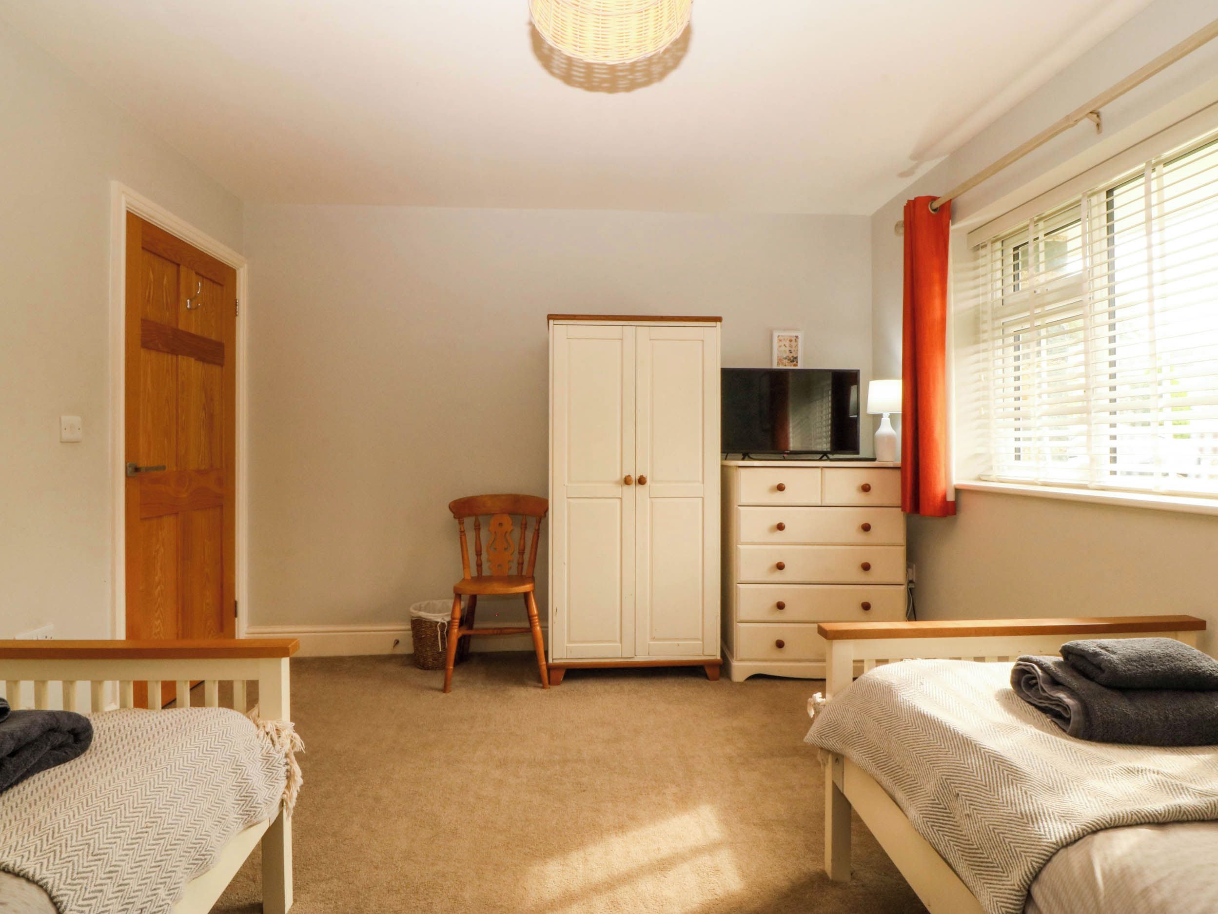A bedroom with two single beds, a wardrobe, a television, and a window with blinds.