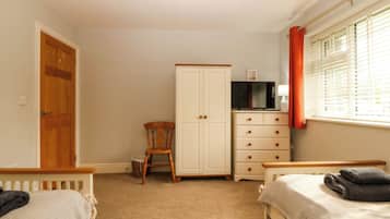 A bedroom with two single beds, a wardrobe, a television, and a window with blinds.