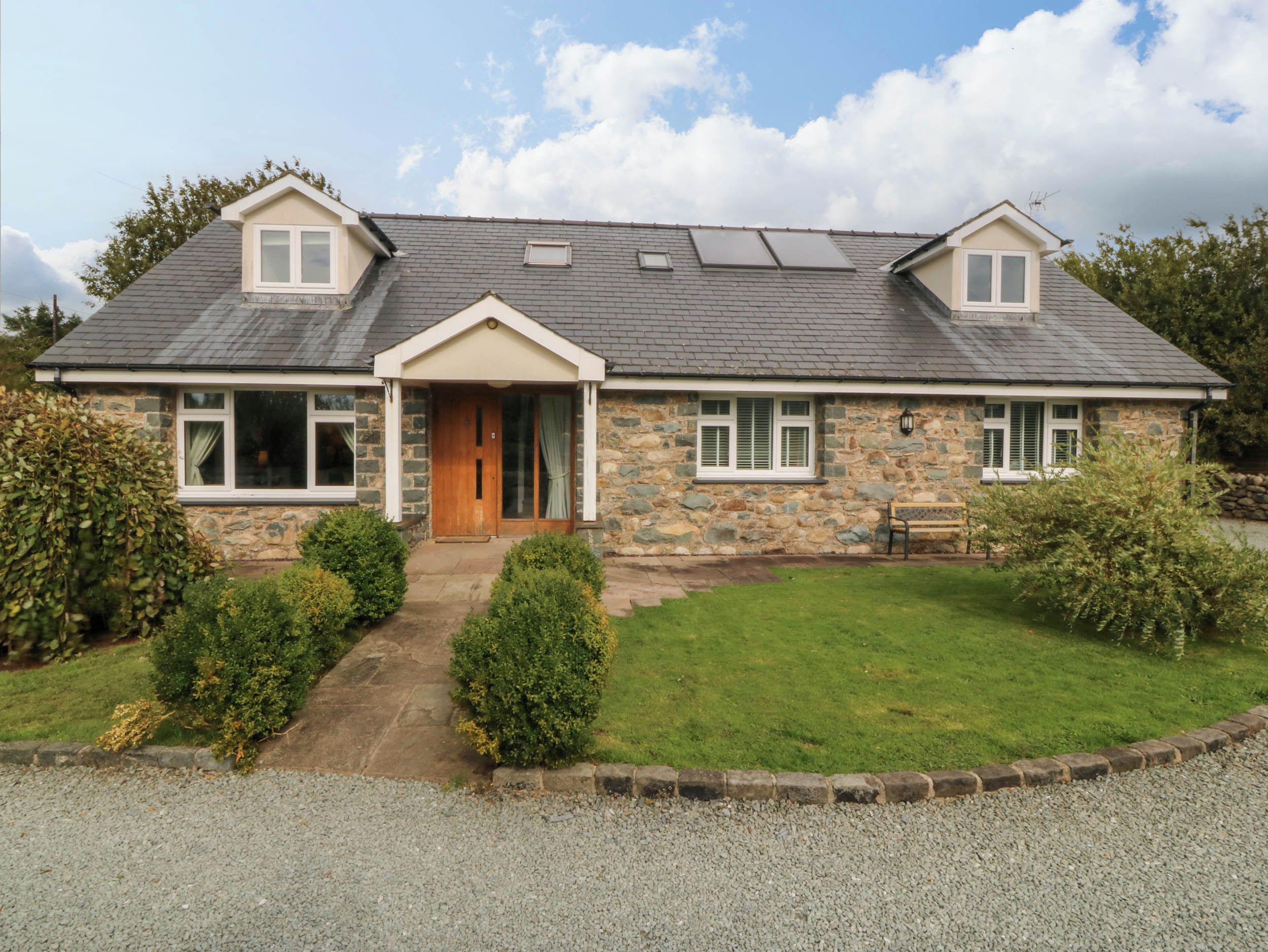 A two-story stone house with a sloped roof, a front porch, and a small garden.