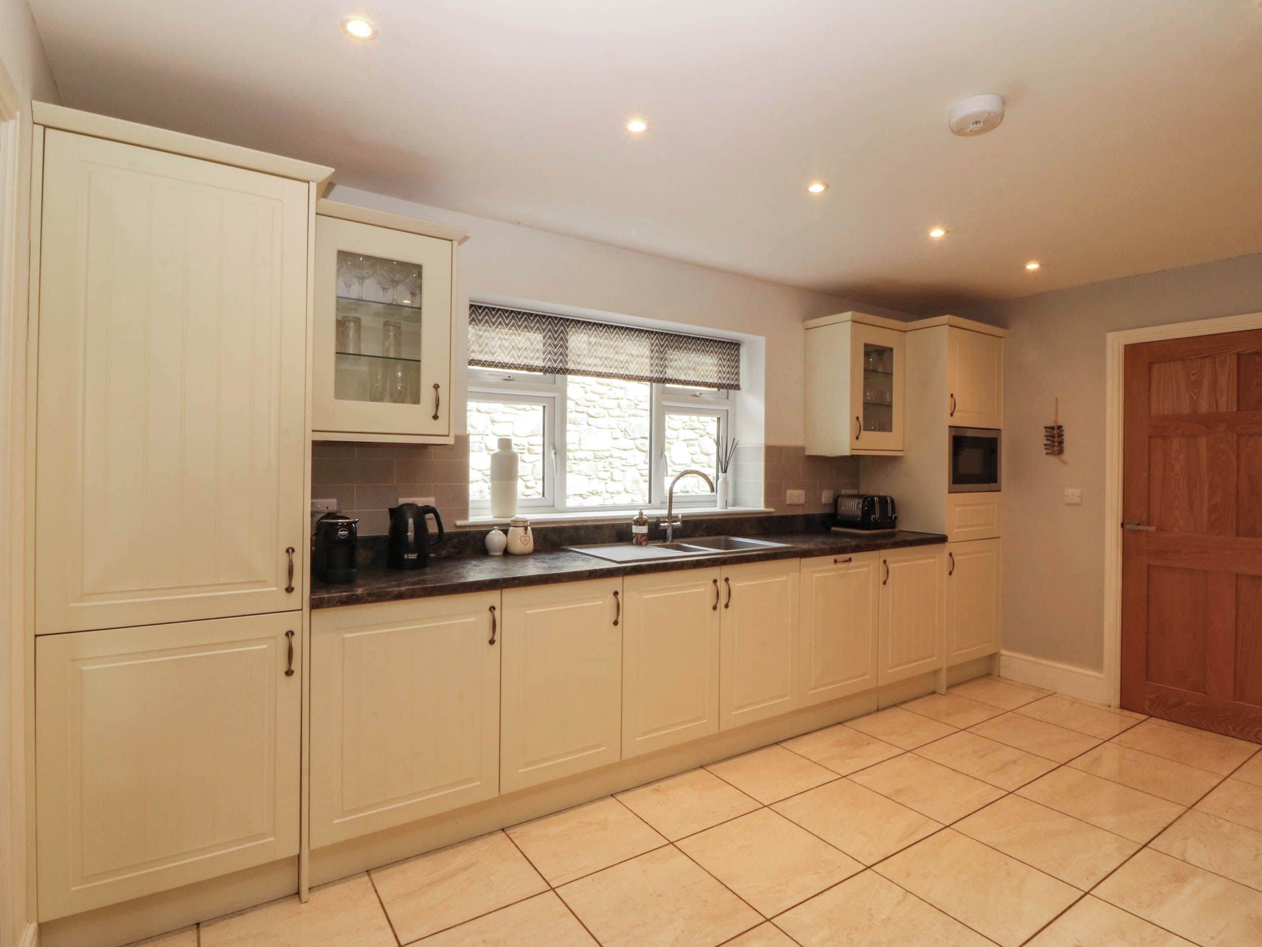 A kitchen with white cabinets, a black countertop, a window with a stone wall, and a wooden door.
