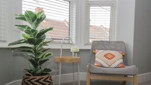 A room with a grey chair, a potted plant, and a small table with a vase of flowers. - 6 Sydney Road (Ramsgate)