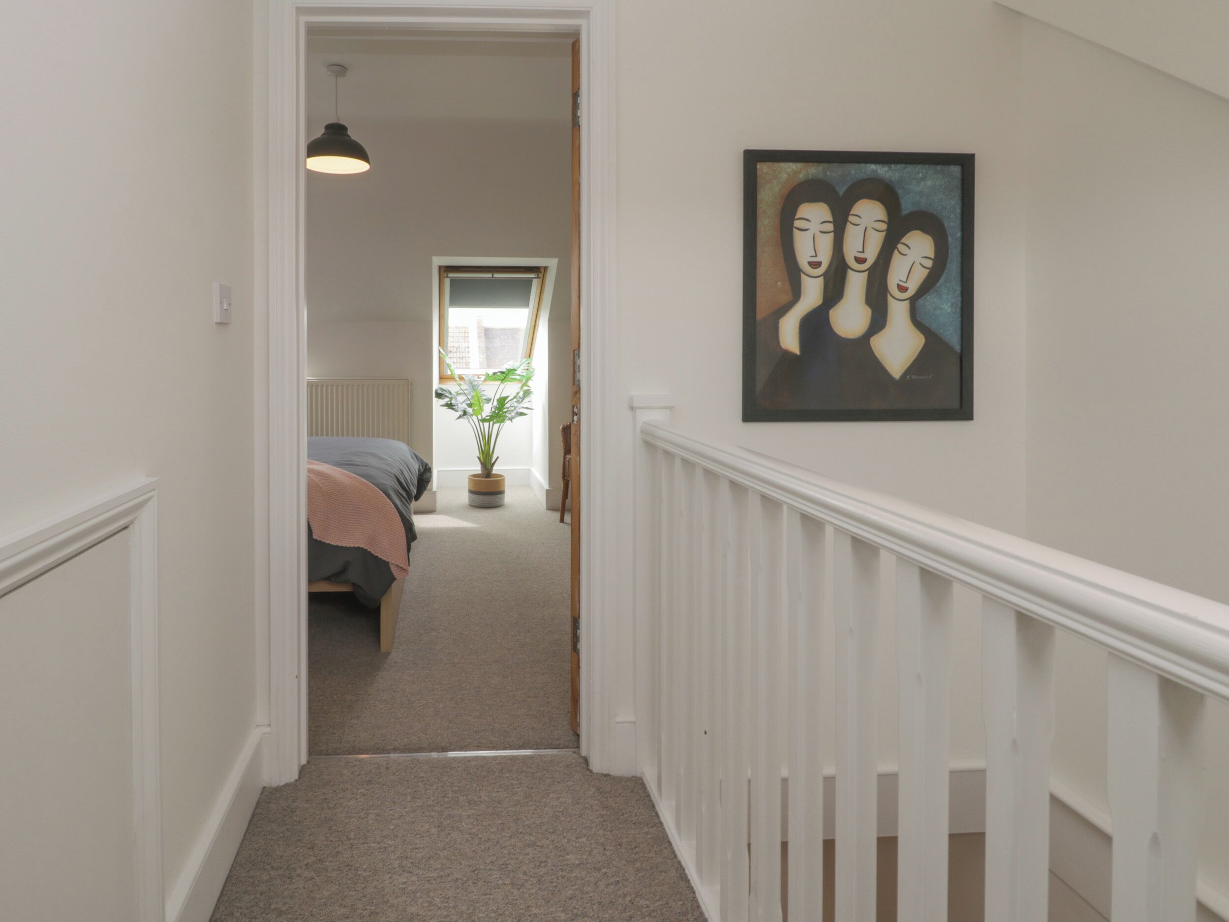 A hallway leading to a bedroom with a bed, a potted plant, and a painting on the wall.