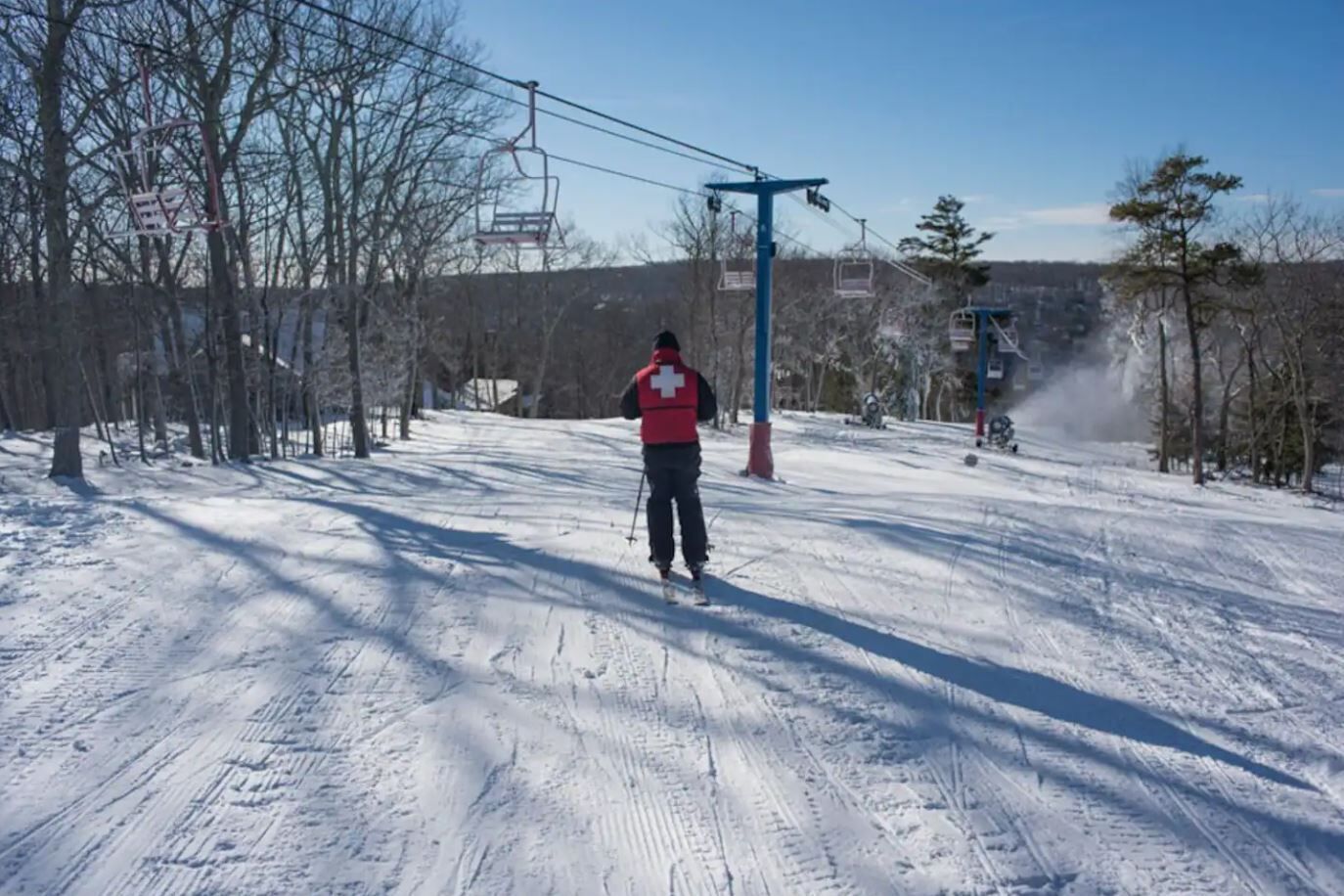 Une personne fait du ski sur une pente enneigée, avec des remontées mécaniques en arrière-plan.