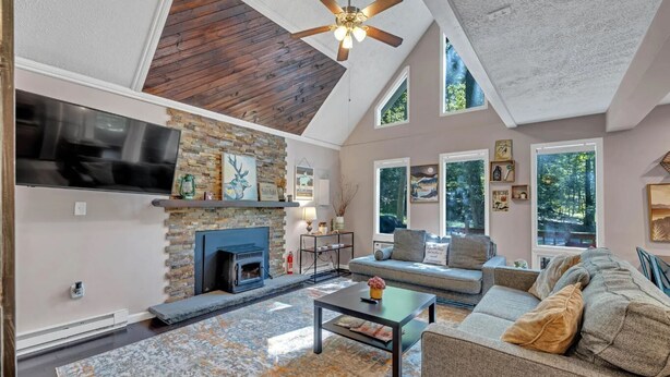 A spacious living room with a stone fireplace, a large flat-screen TV, and a ceiling fan.
