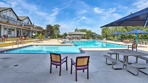 A pool area with lounge chairs and umbrellas, a building with a balcony, and a clear blue sky.