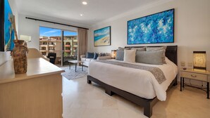 A modern hotel room with a large bed, a desk, a chair, and a view of the city through the balcony doors. - Beachfront, Premium Ocean View, 5 Star (Cabo San Lucas)