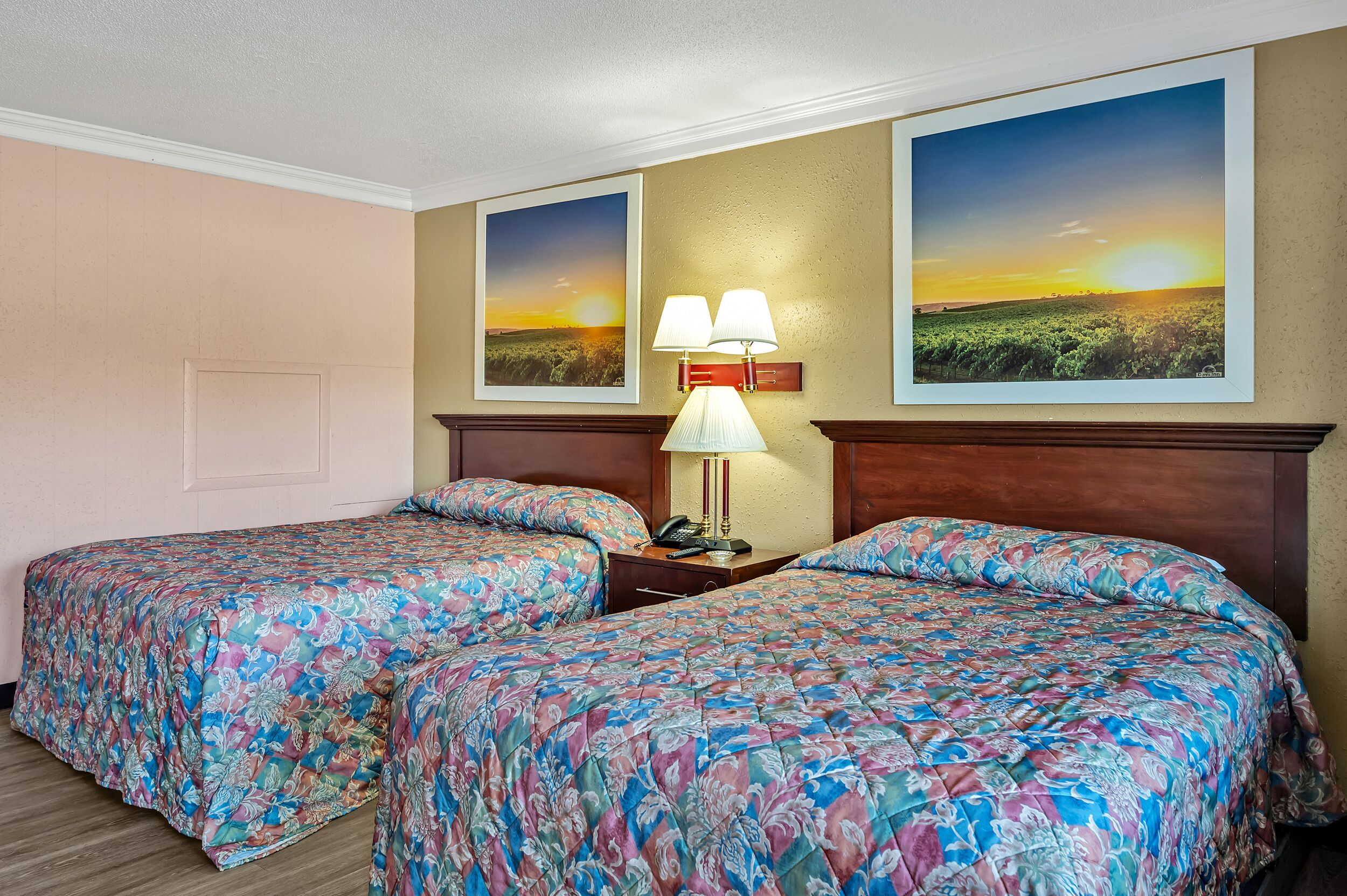 A hotel room with two beds, a nightstand with a lamp, and two framed pictures on the wall.