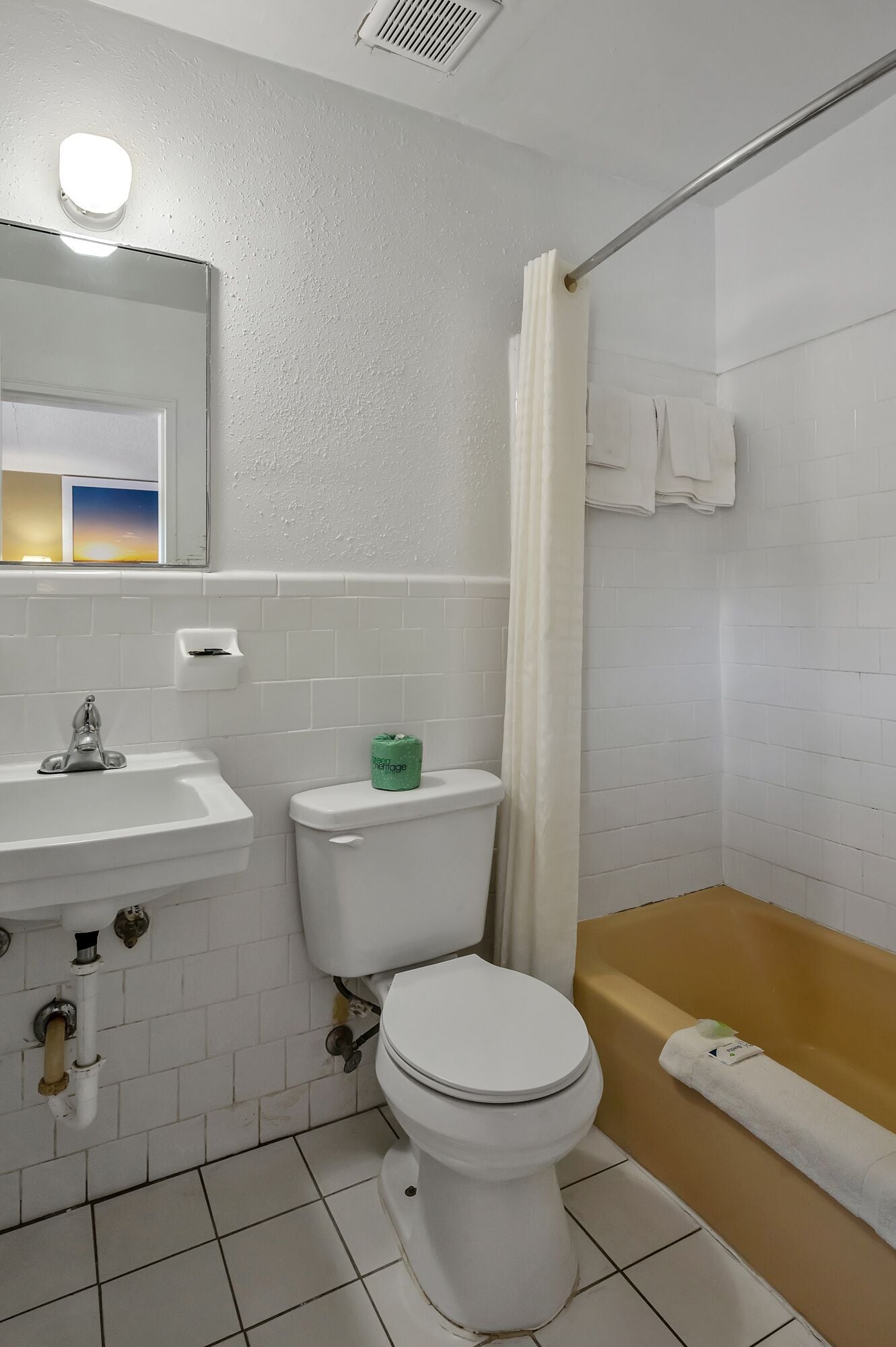 A bathroom with a white sink, toilet, and bathtub. There is a green toilet paper holder and a towel rack with towels.
