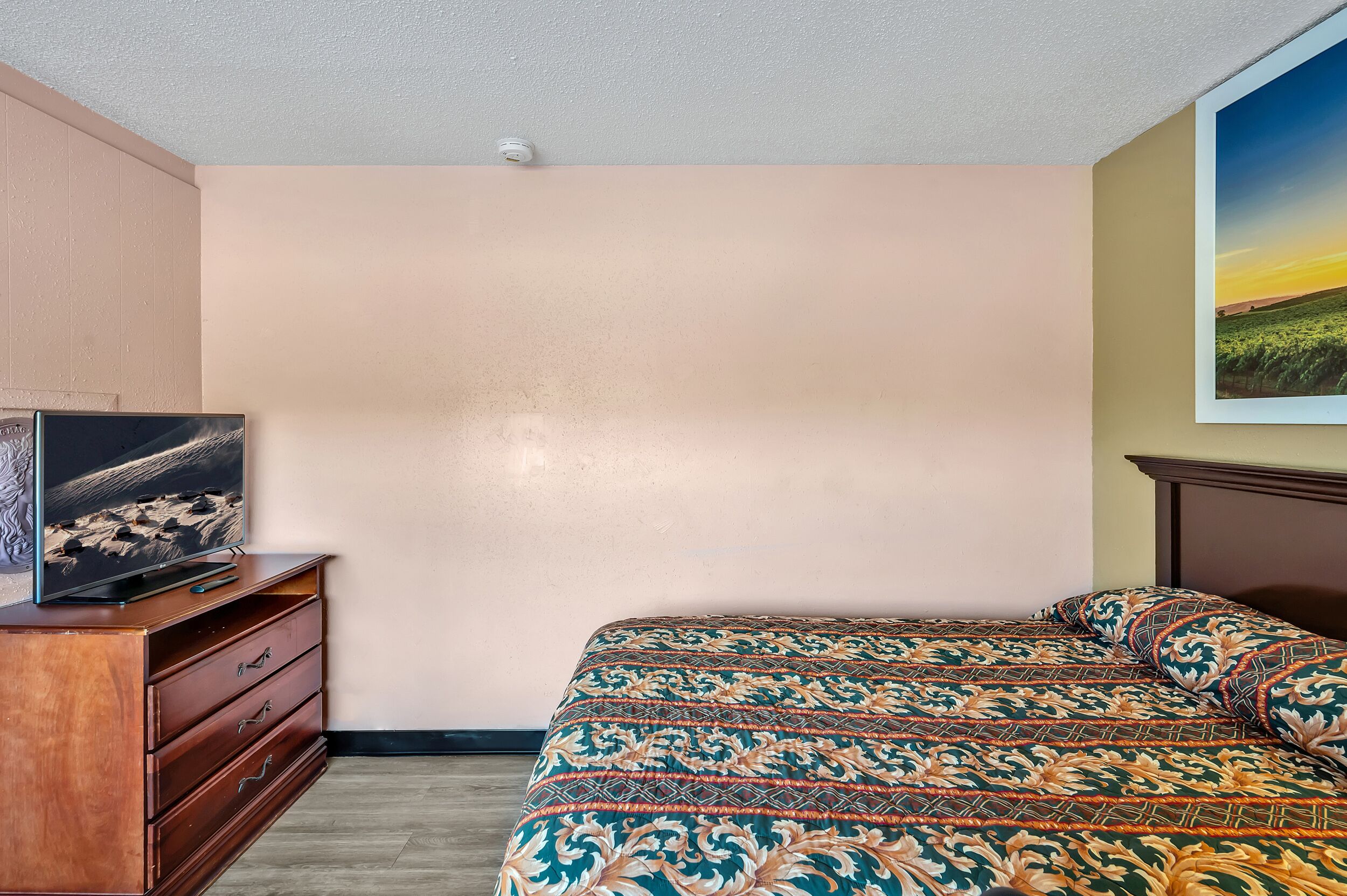 Een slaapkamer met een bed, een dressoir en een televisie op een standaard.