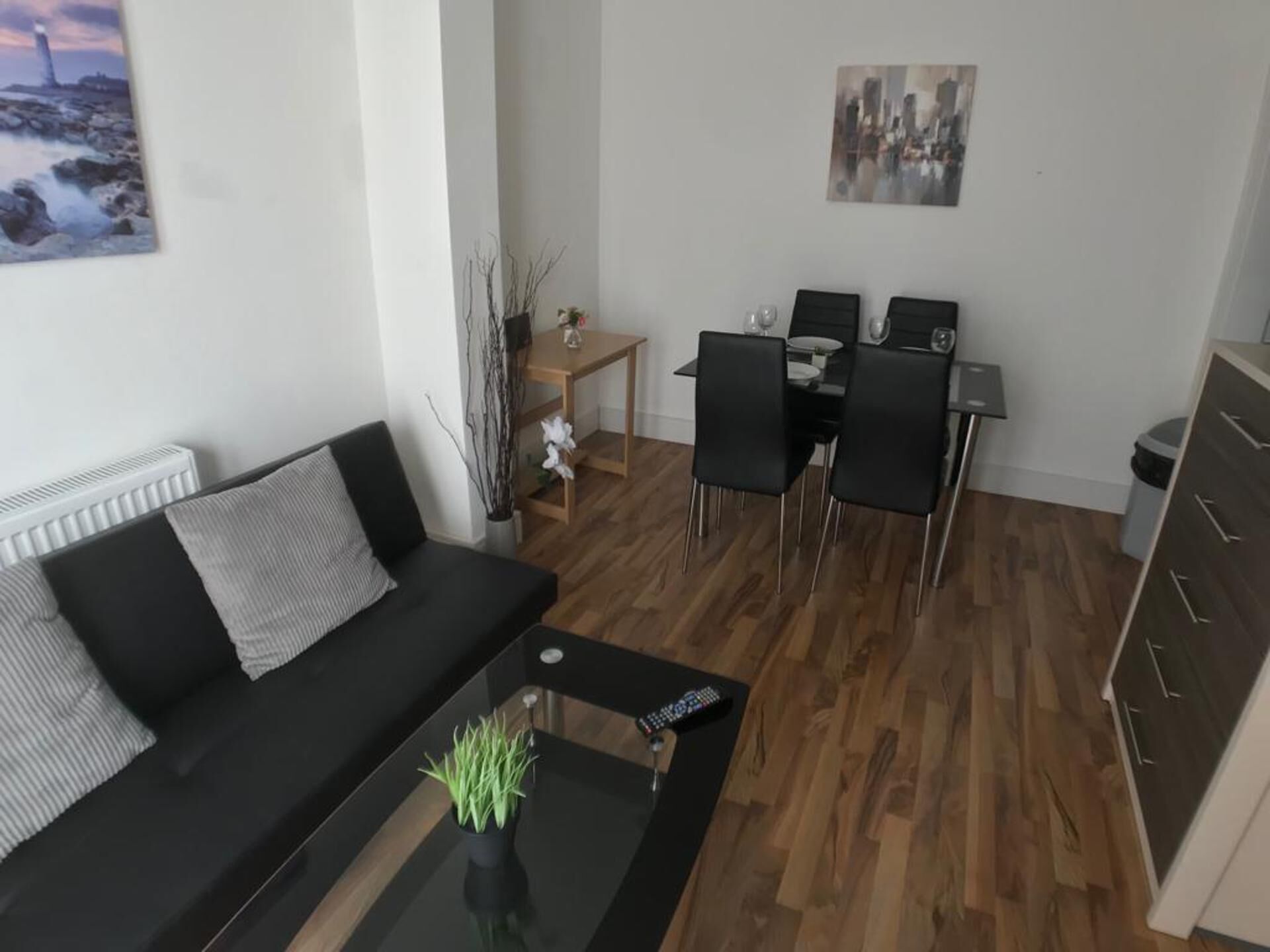 A modern living room with a black sofa, a glass coffee table, and a dining area with a wooden table and black chairs.