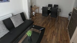 A modern living room with a black sofa, a glass coffee table, and a dining area with a wooden table and black chairs. - Bermondsey London, 3 People Apartment, Peaceful (London)