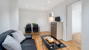 A modern living room with a black leather sofa, a glass coffee table, and a dining area with a table and chairs. - Bermondsey London, 3 People Apartment, Peaceful (London)