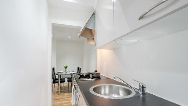 A modern kitchen with a stainless steel sink, black countertop, and wooden flooring. - Bermondsey London, 3 People Apartment, Peaceful (London)