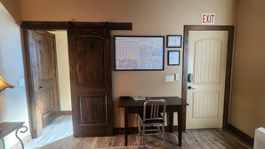 Un couloir avec une porte en bois, un bureau avec une chaise, une lampe et un calendrier fixé au mur.