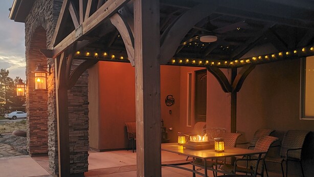 Un patio couvert avec des murs en pierre, une pergola en bois et des guirlandes lumineuses.