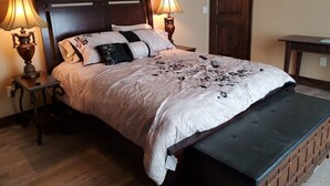 Un lit bien fait, avec une tête de lit en bois, deux lampes de chevet et un banc au pied du lit.