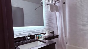 A modern bathroom with a large mirror, a sink, a toilet, and a shower area.