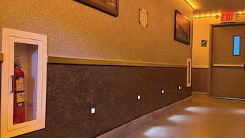 A hotel corridor with a fire extinguisher, exit sign, and framed pictures on the walls.