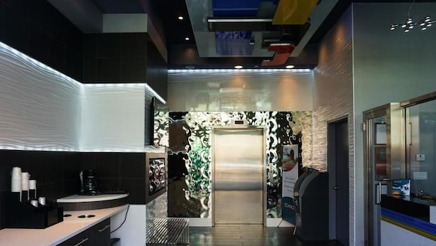 A modern hotel lobby with a sleek design, including a reception desk, a counter with a coffee machine, and a patterned wall.