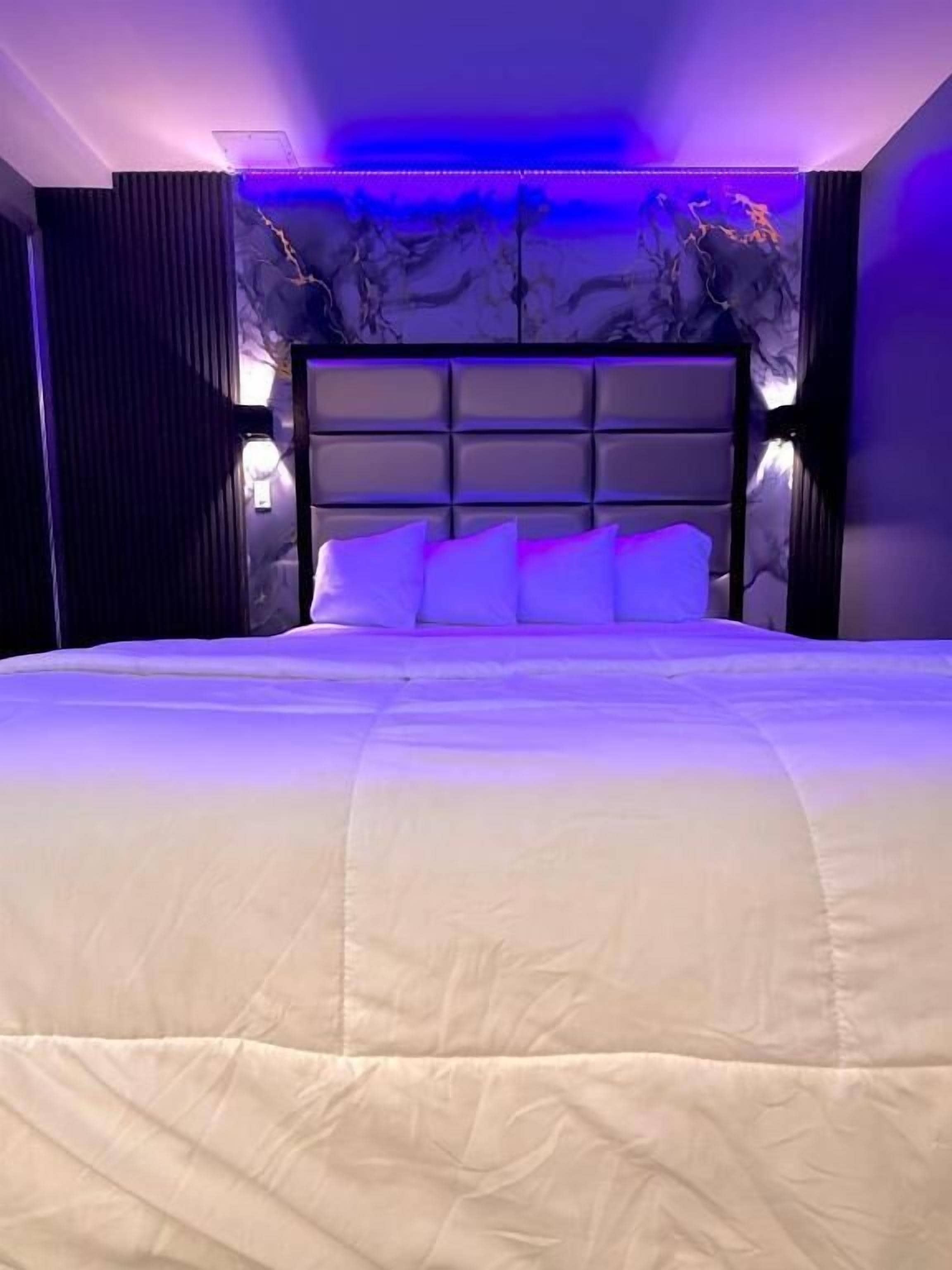 A bedroom with a large bed, a headboard with multiple panels, and wall-mounted lighting.