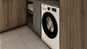 Kompakti pyykinhuone, jossa on etuaukollinen pesukone, puukaapit ja laatoitettu lattia.