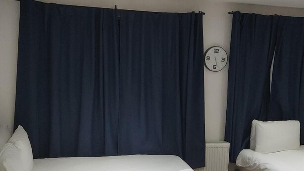 Hotellihuoneessa on suuri sänky, pienempi sänky, yöpöytä, kello ja patteri.