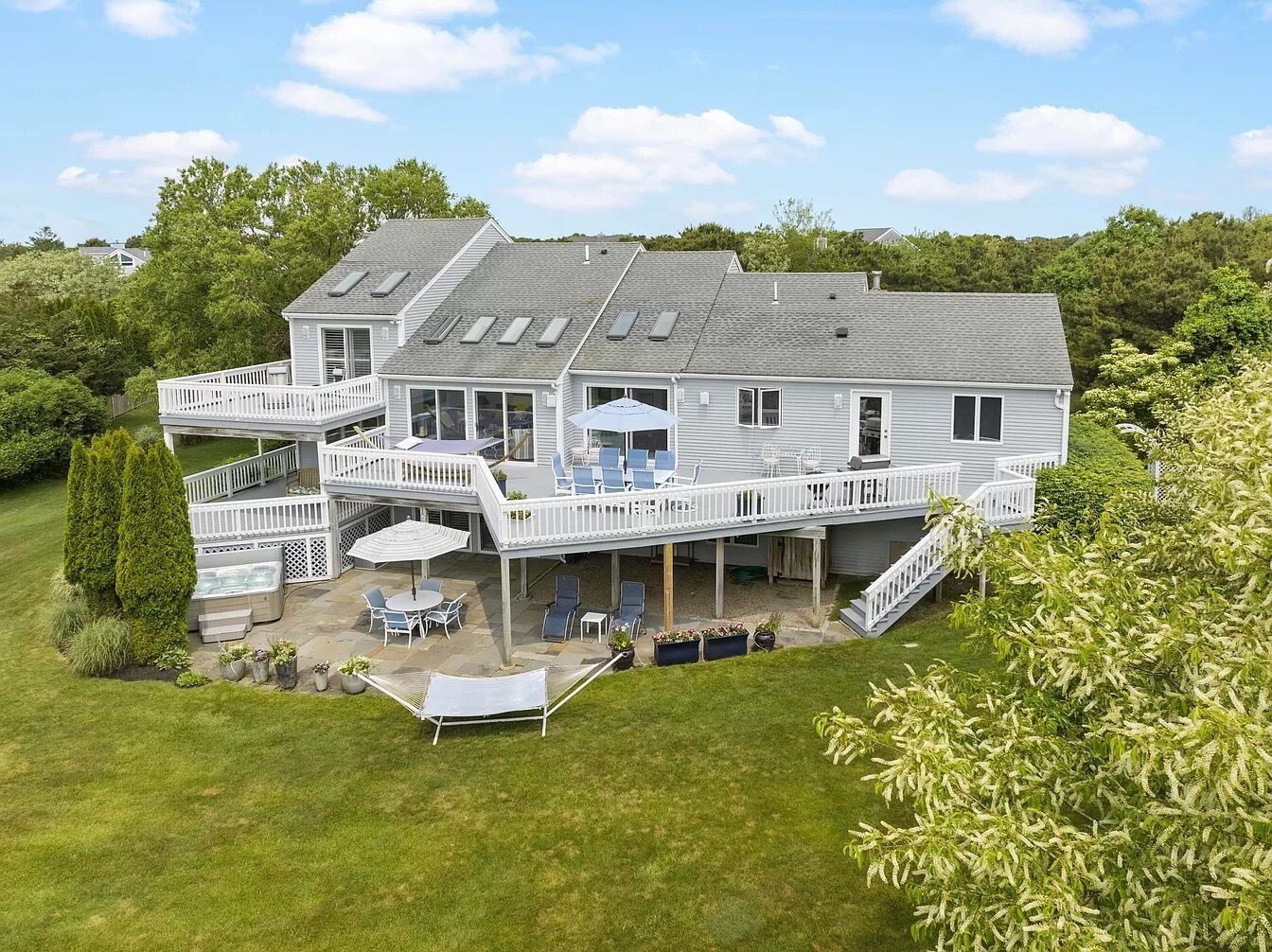 A two-story house with a covered patio, outdoor seating, and a hot tub.