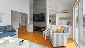 A modern living room with a fireplace, a television, and a dining area. - Beach Getaway - Spacious Katama Beach House (Edgartown)
