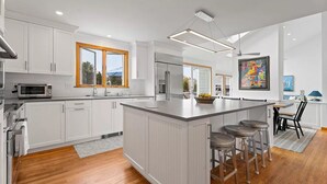 A modern kitchen with white cabinetry, a central island with bar stools, a microwave, and a refrigerator. - Beach Getaway - Spacious Katama Beach House (Edgartown)