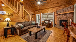 A wooden cabin interior with a staircase, a fireplace, a sofa, and a coffee table.
