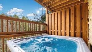 A hot tub on a wooden deck with a clear view of the surrounding trees and sky.