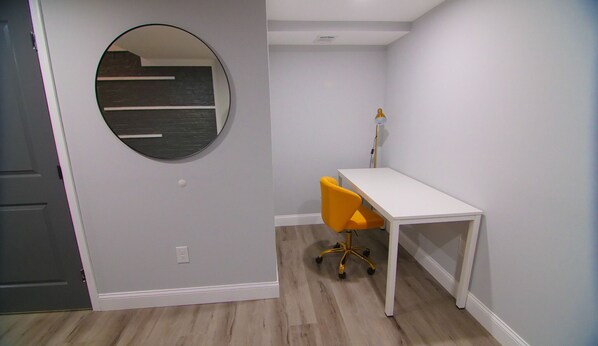 A small, modern room with a white desk, a yellow chair, and a round mirror on the wall. - Lux Stay near Patterson Park, John Hopkins, & Stadiums! Family & Pet-Friendly. (Baltimore)