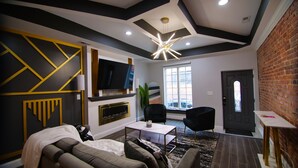 A modern living room with a fireplace, a flat-screen TV, and a seating area with sofas and chairs. - Lux Stay near Patterson Park, John Hopkins, & Stadiums! Family & Pet-Friendly. (Baltimore)