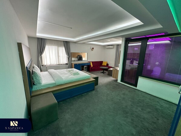 Une chambre d’hôtel moderne avec un lit, un bureau, un canapé rouge et une grande fenêtre avec des rideaux.