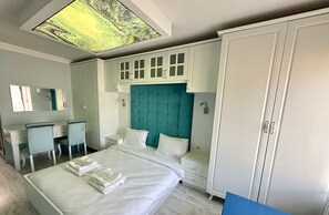 A hotel room with a bed, a desk, a chair, a wardrobe, and a skylight.