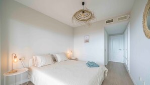A bedroom with a large bed, two bedside tables with lamps, a woven ceiling light, a framed picture on the wall, and a door leading to another room. - Casa Jsmina Calahonda With Seaview 2 bed 2 Bath (Sitio de Calahonda)