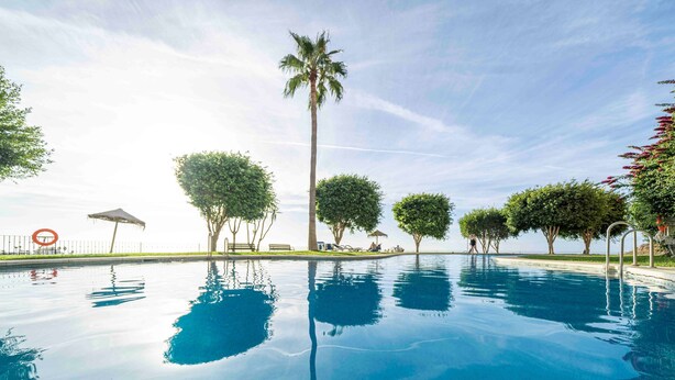 A swimming pool with clear blue water, surrounded by trees and a bench. - Casa Jsmina Calahonda With Seaview 2 bed 2 Bath (Sitio de Calahonda)